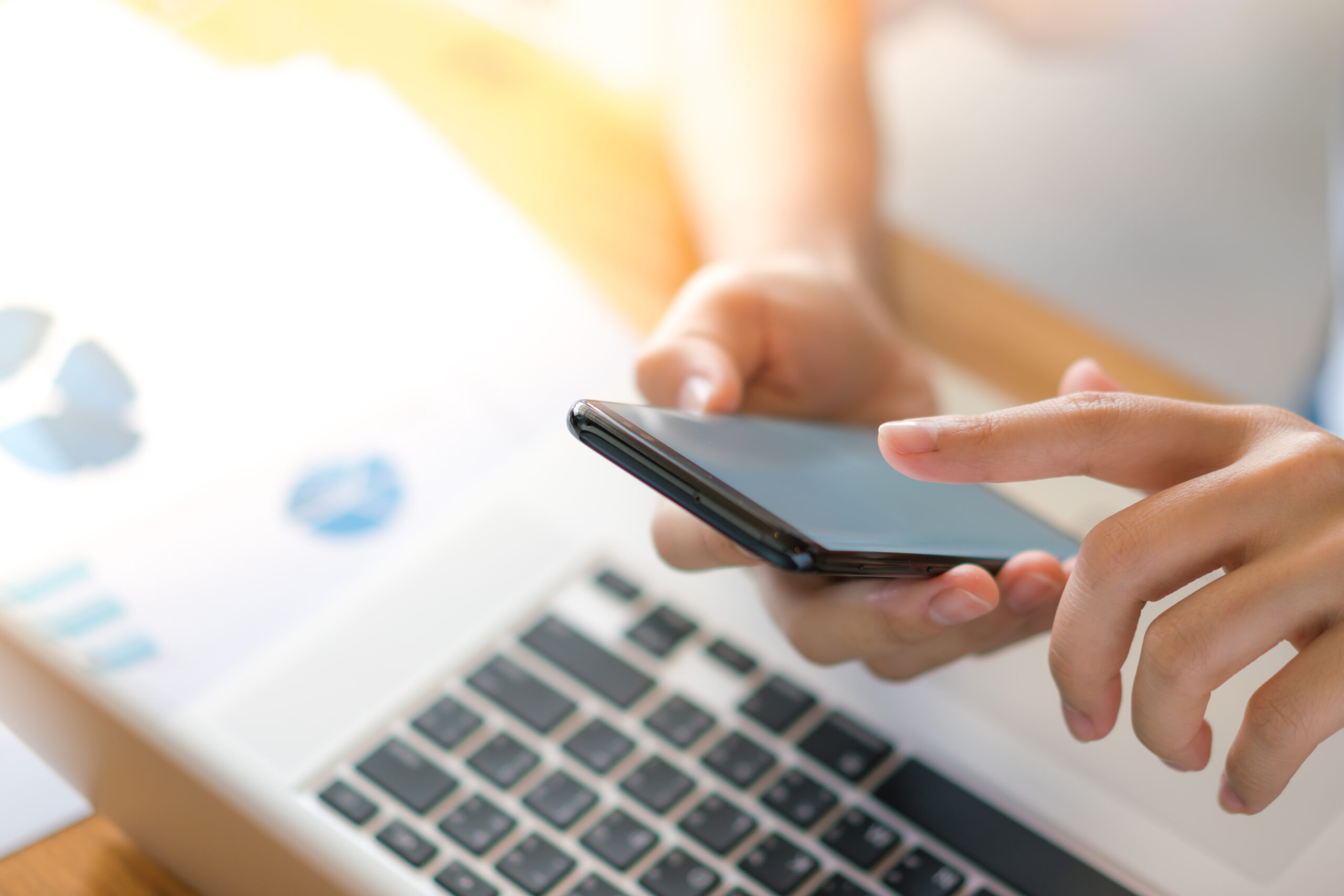 Business woman hand with Financial charts and mobile phone over laptop on the table